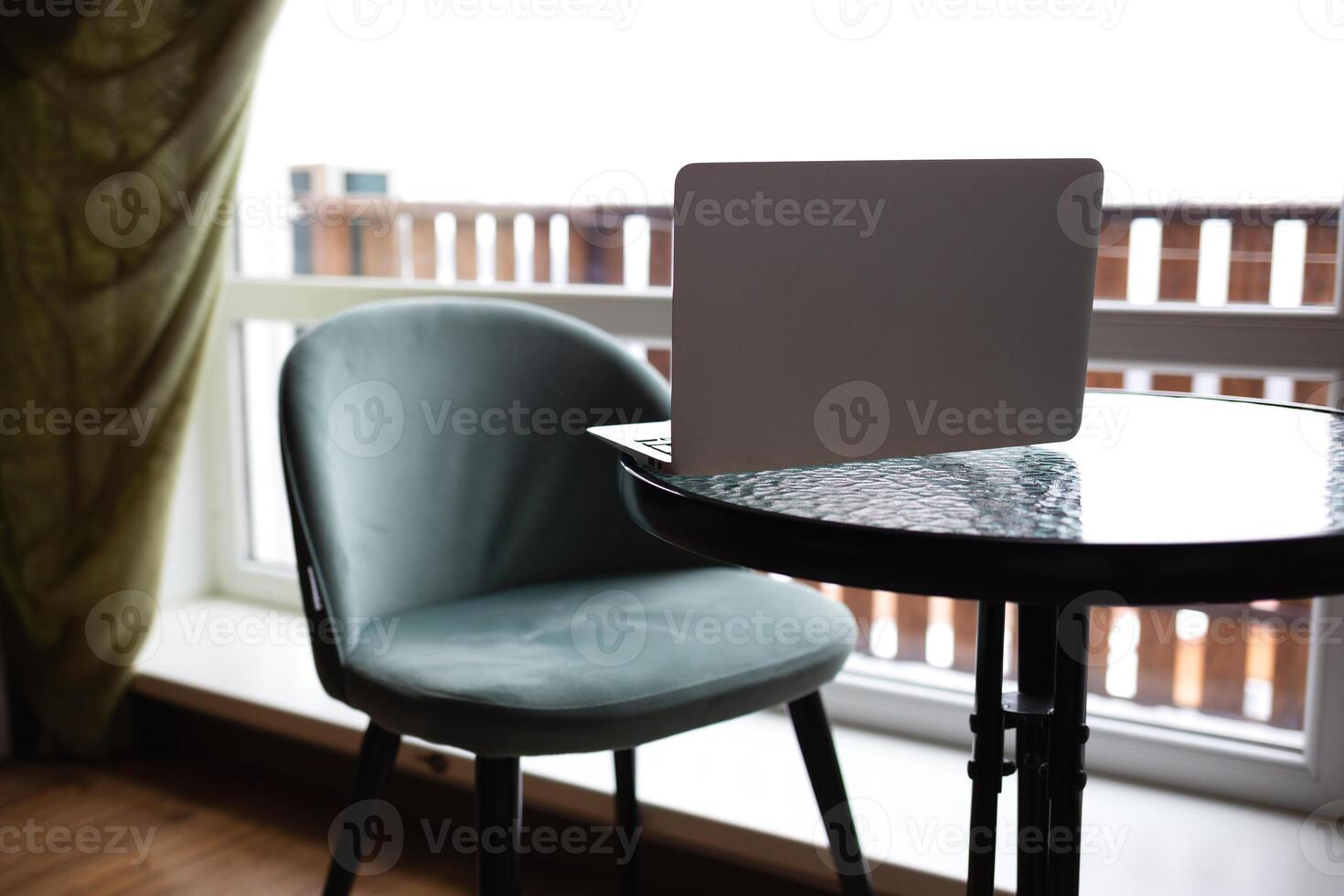 Close-up of a table with a laptop and a chair in front of a large window. remote work concept photo