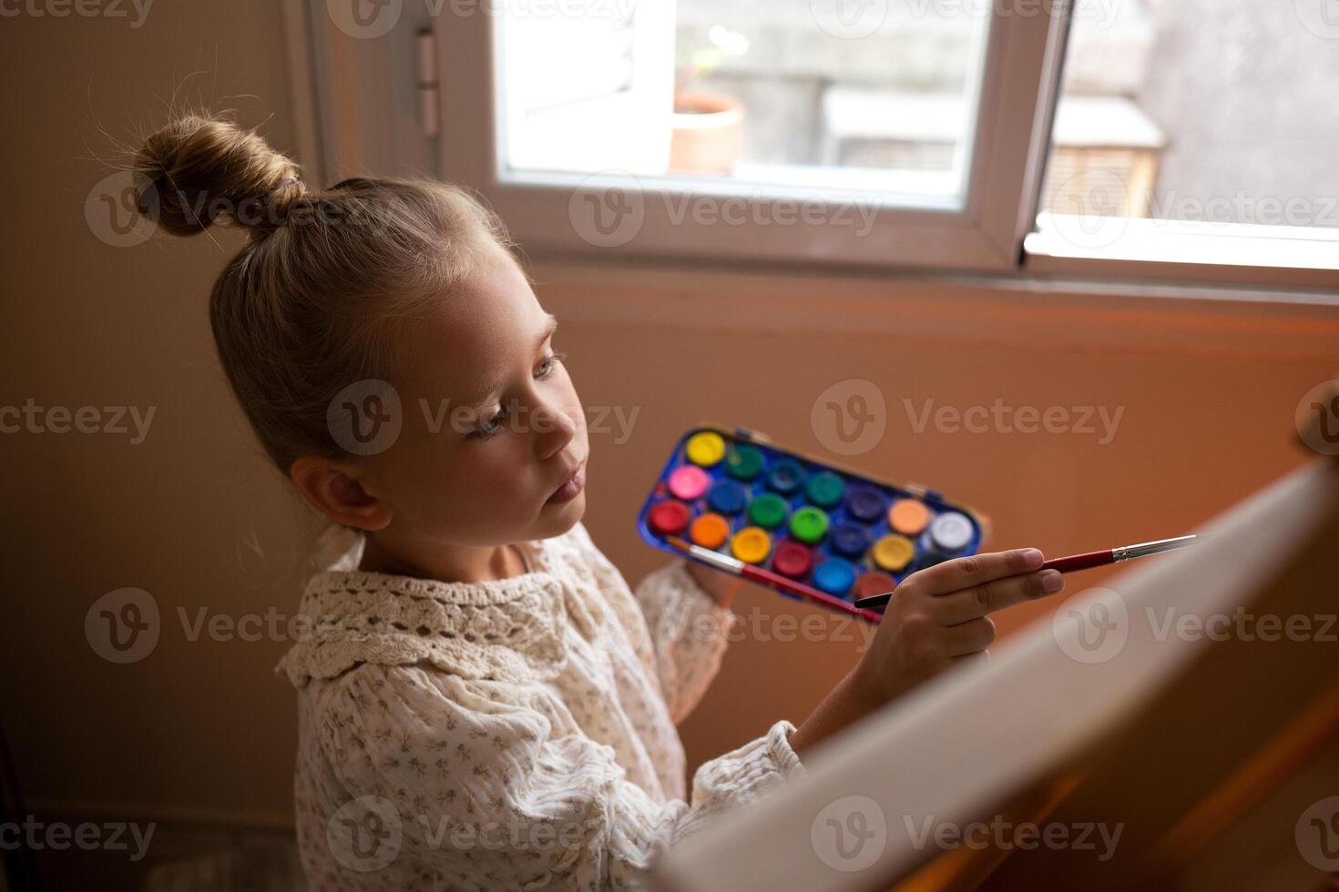 little cute girl draws with paints on canvas at the easel photo