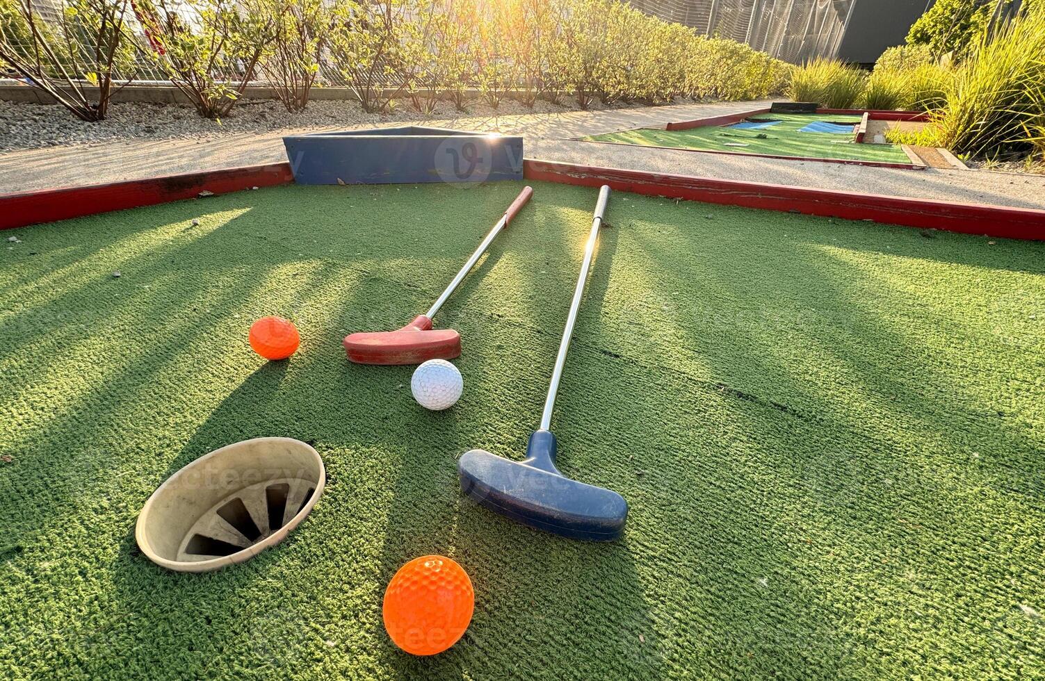 Assorted miniature golf putters and balls askew on synthetic grass. photo