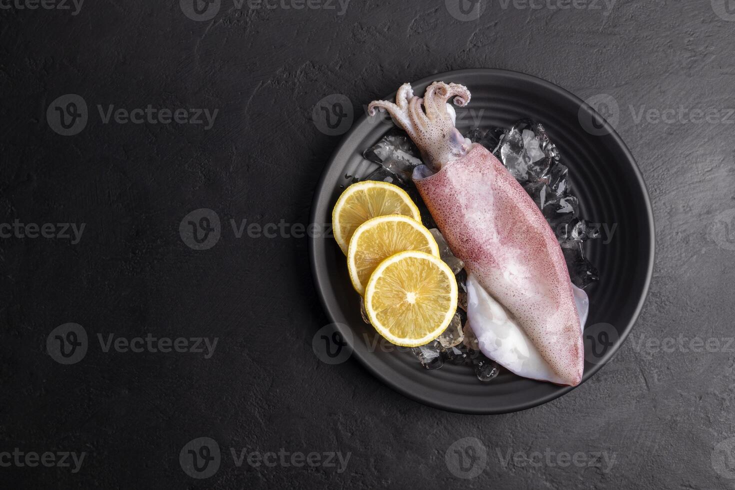 Fresh raw squid. Raw squid on a black plate with ice. Lemon slices. Top view and copy space for your text. photo