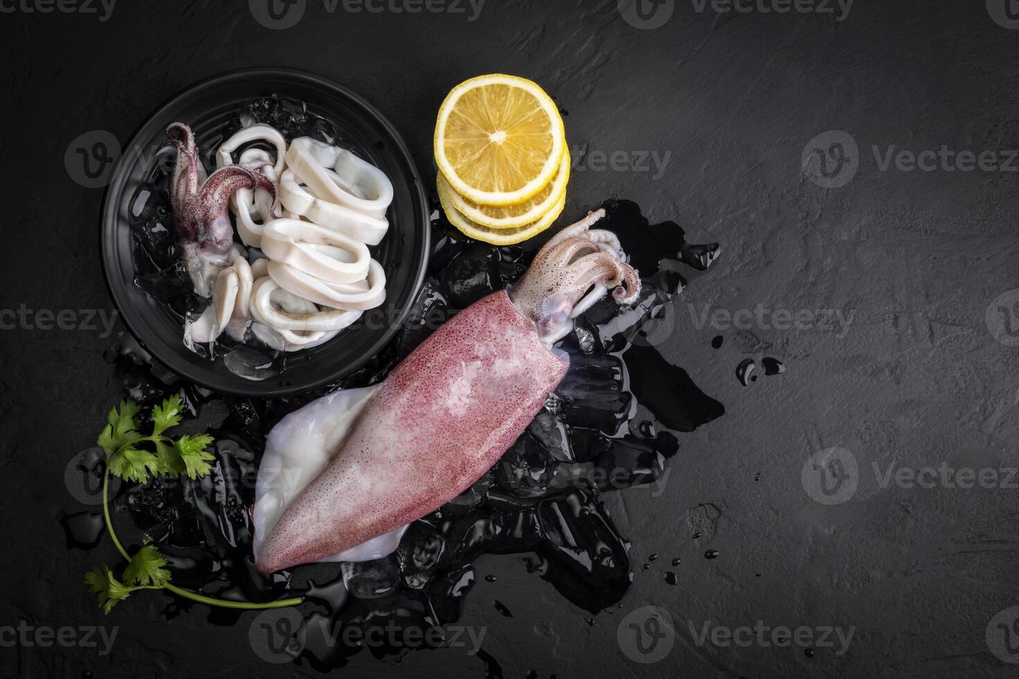Fresh raw squid. Raw squid on a black plate with ice. Lemon slices. Top view and copy space for your text. photo