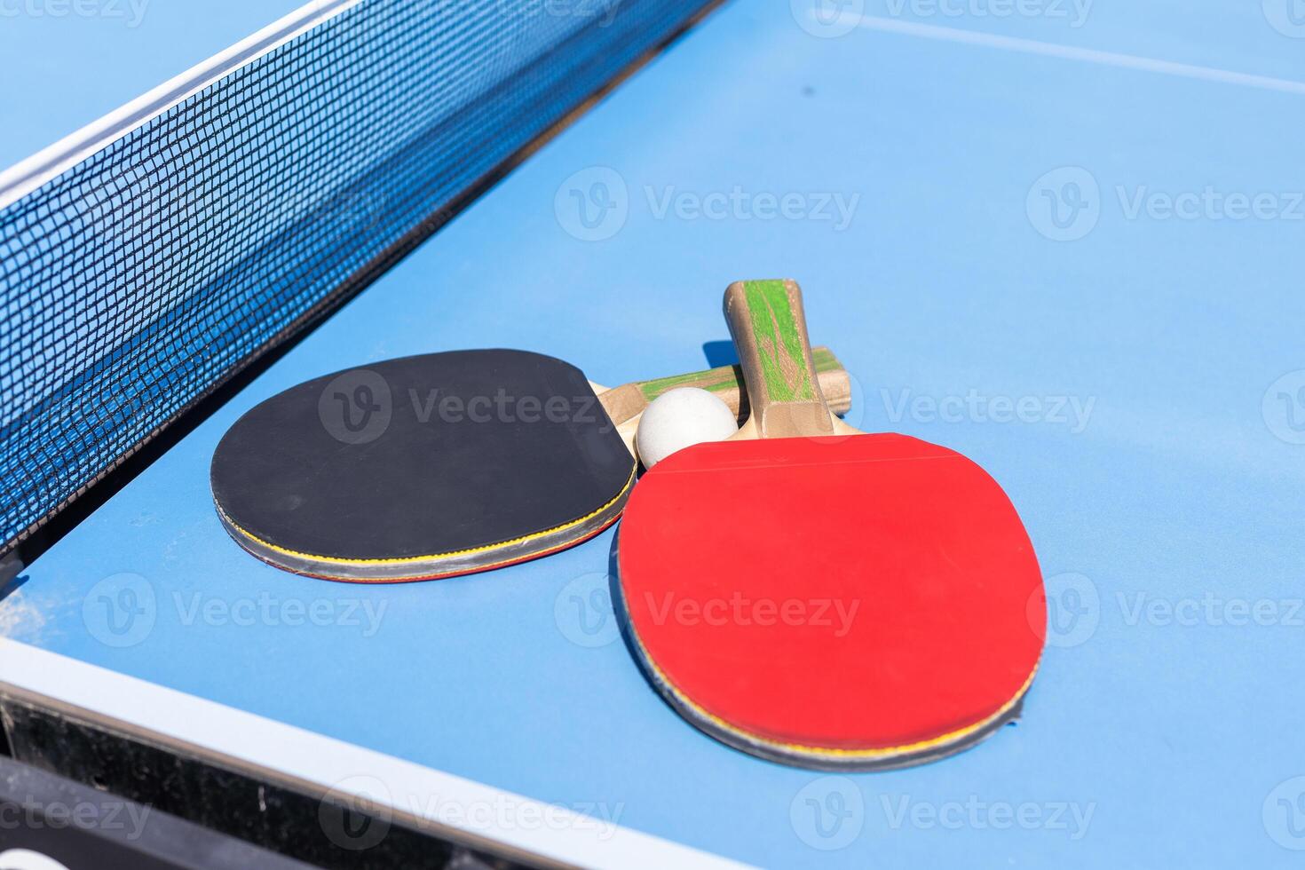 Two table tennis or ping pong rackets and ball on blue table with net photo