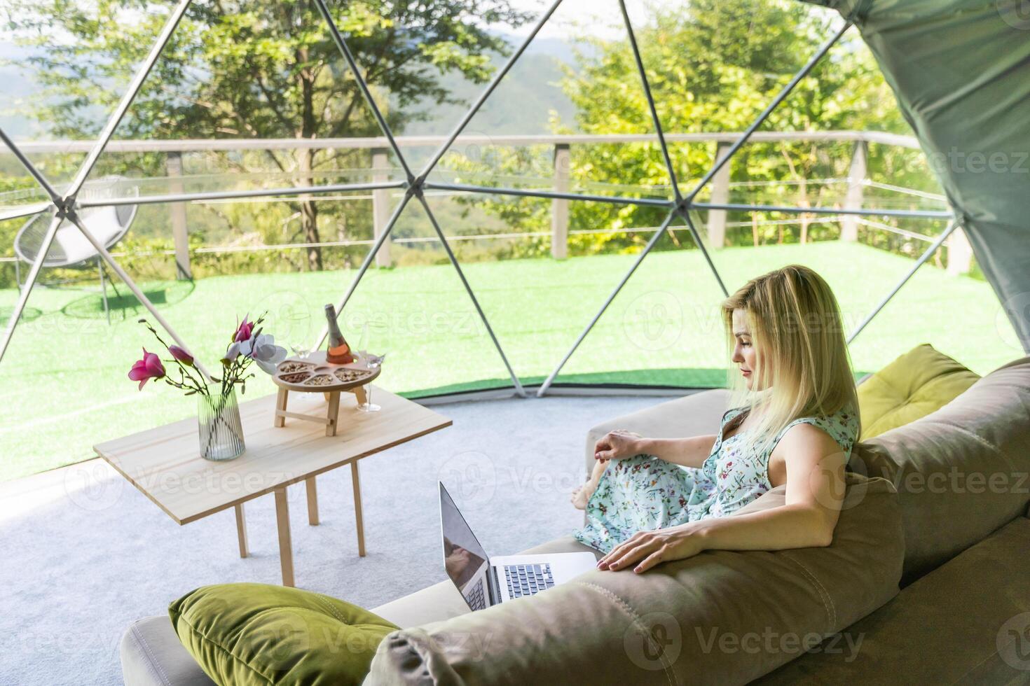 Young caucasian woman using and watching on laptop computer on in dome camping hotel. Tourism, vacation and weekend. photo