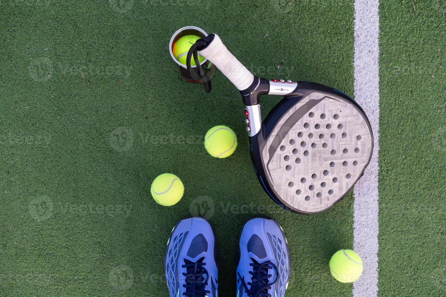 Yellow balls on grass turf near padel tennis racket behind net in green court outdoors with natural lighting. Paddle is a racquet game. Professional sport concept with copy space. photo