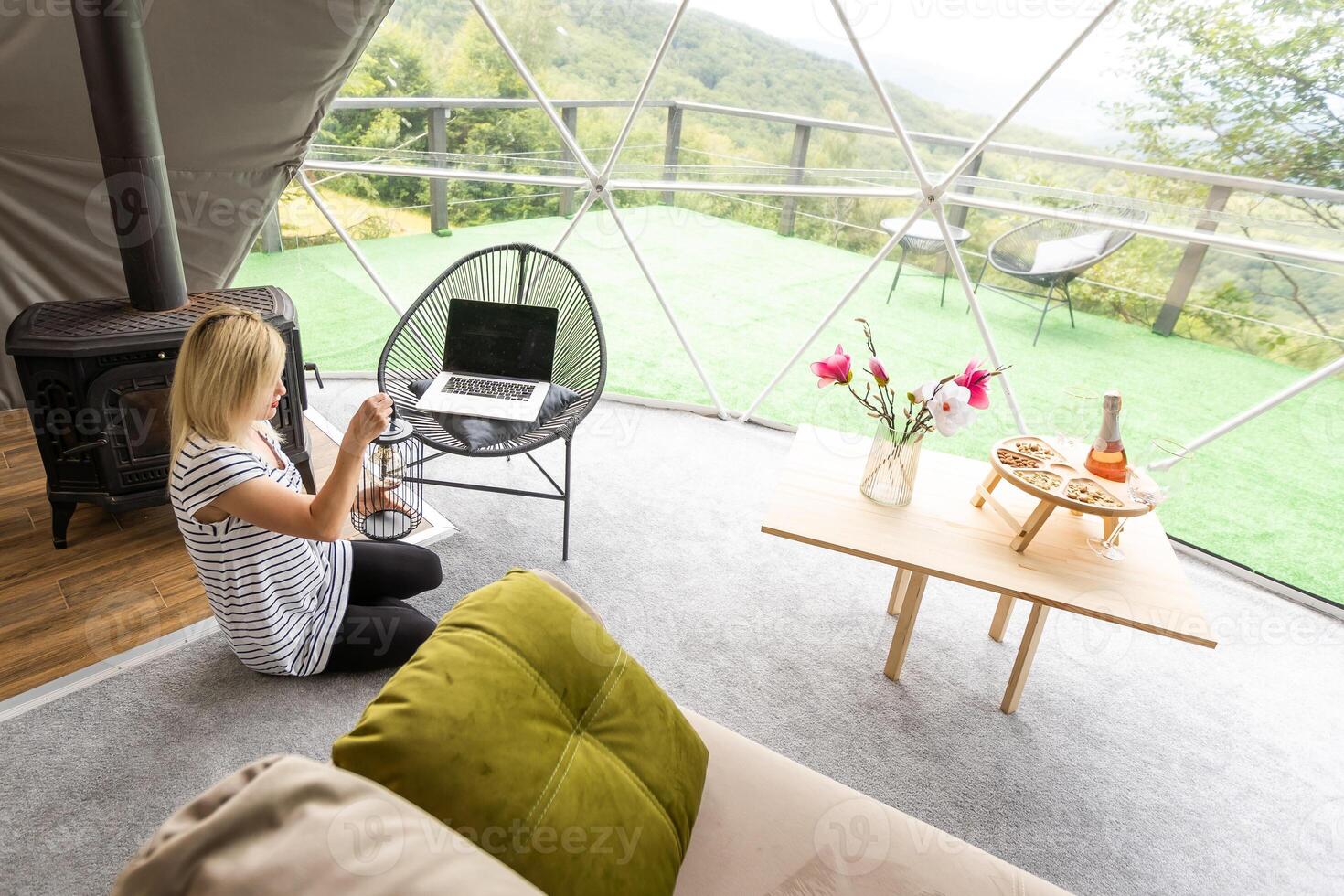 Happy young woman chatting online by using laptop in dome camping. Glamping vacation concept photo