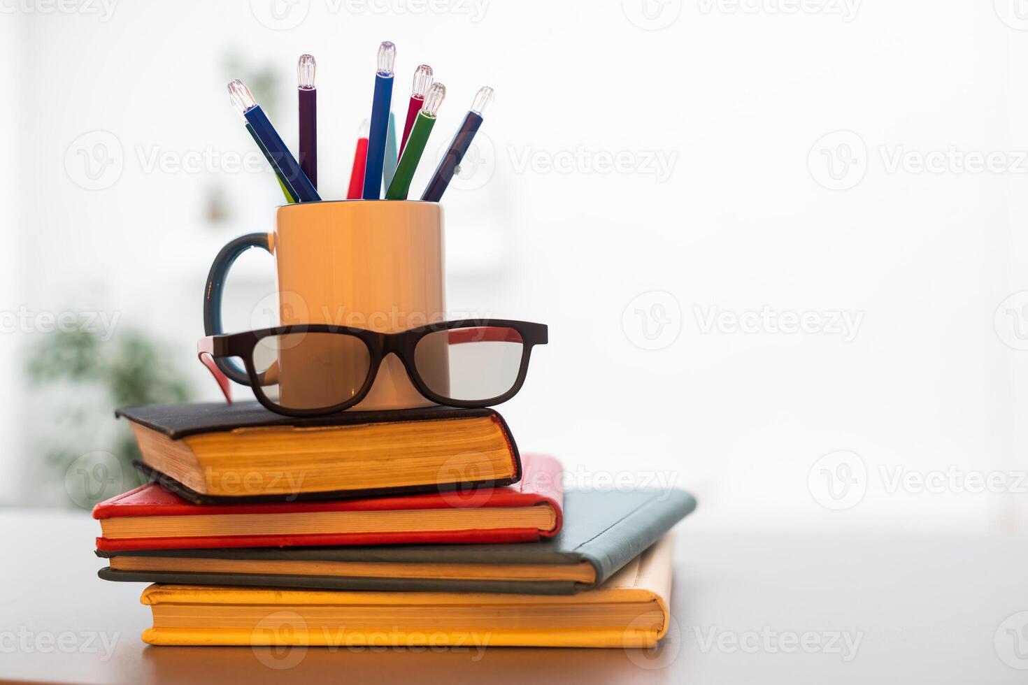 Stack of books with colored spines, colorful pencils in a cup photo