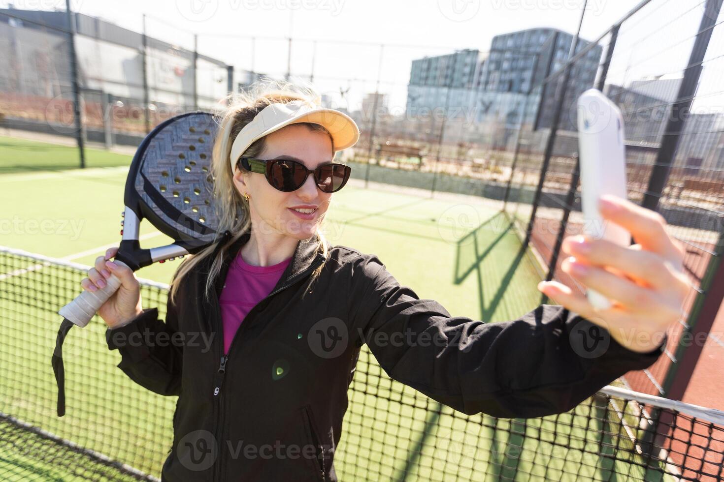 Young female smiling and looking at camera while playing padel against green background photo