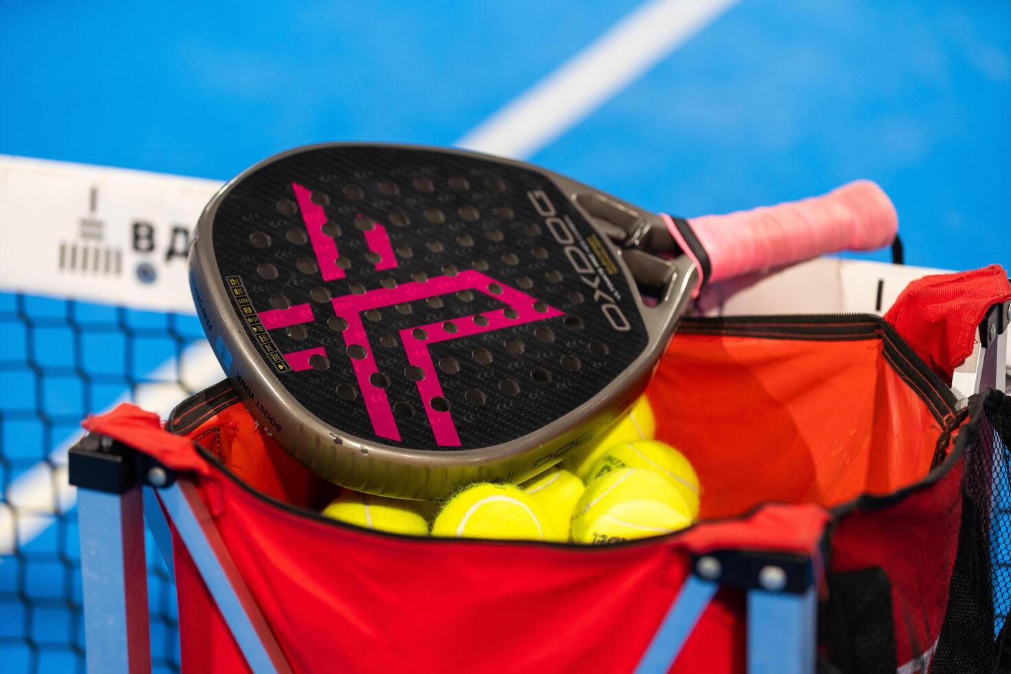 Kyiv, Ukraine, April 18, 2024. Black professional paddle tennis racket and ball with natural lighting on blue background. Horizontal sport theme poster, greeting cards, headers, website and app photo