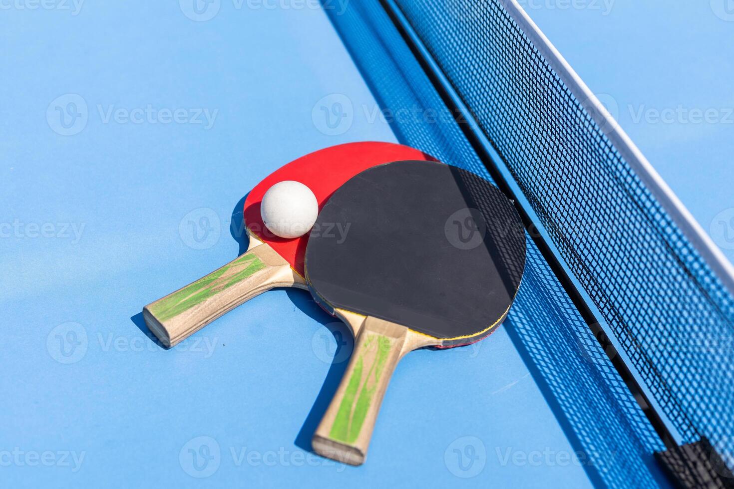 Two table tennis or ping pong rackets and ball on blue table with net photo