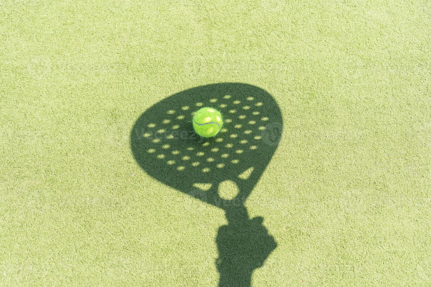 Shadow of a padel racket with a yellow ball on the green grass. photo