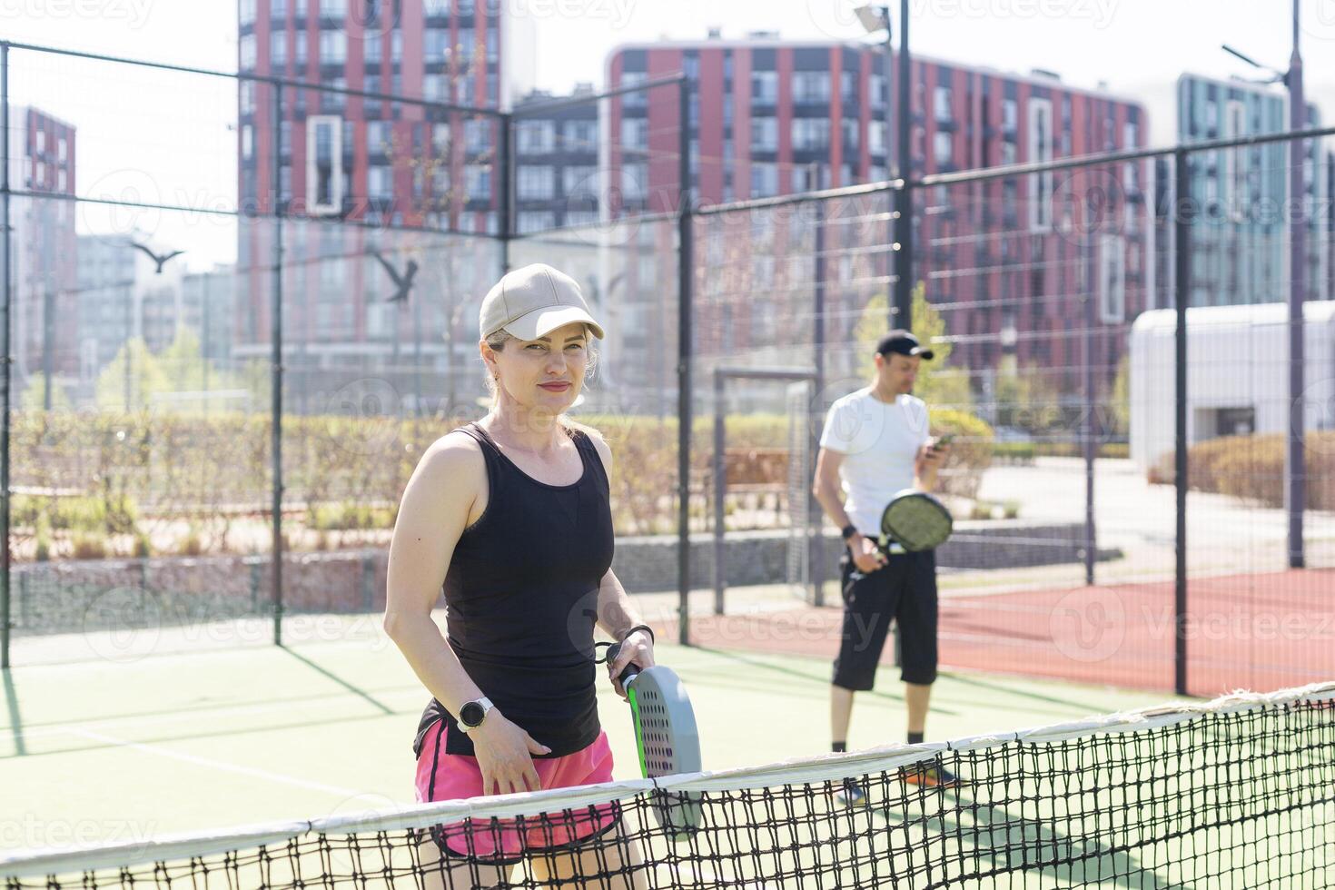 Portrait of positive young woman and adult man standing on padel tennis court, holding racket and ball, smiling photo