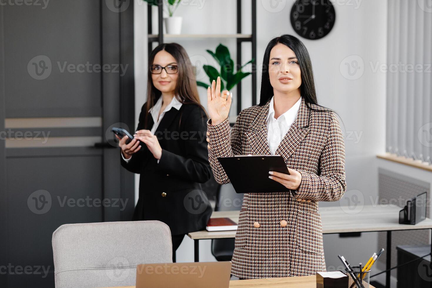 Two young attractive women are working in the office. A woman is talking on the phone, and her colleague is making notes in a notebook photo