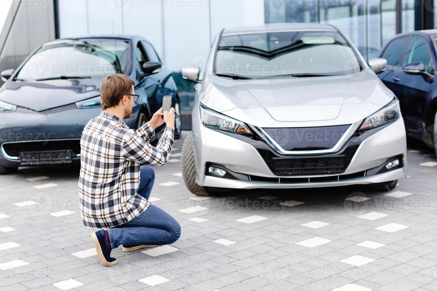 Man customer taking photo to mobile phone chooses auto and wants to buy new car in showroom
