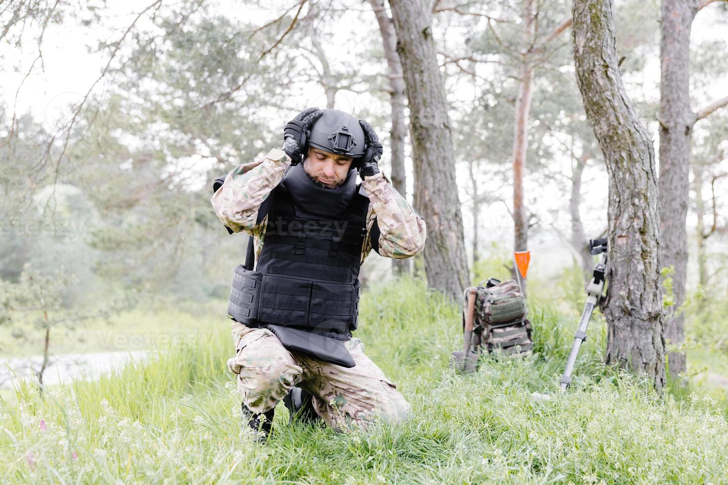 A man in a military uniform and a bulletproof vest works in the forest to demine the territory. A man puts on a protective helmet before starting work photo