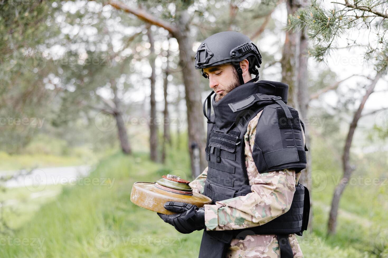 A man in a special suit works with a detector and found an explosive device. A man tries to neutralize an anti-tank mine photo