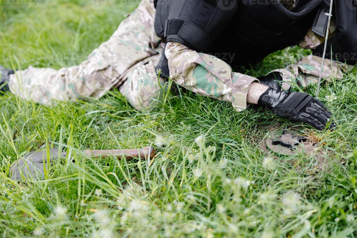 A man in a military uniform and a bulletproof vest works in the forest to demine the territory. A man warns of danger by making a red mark photo