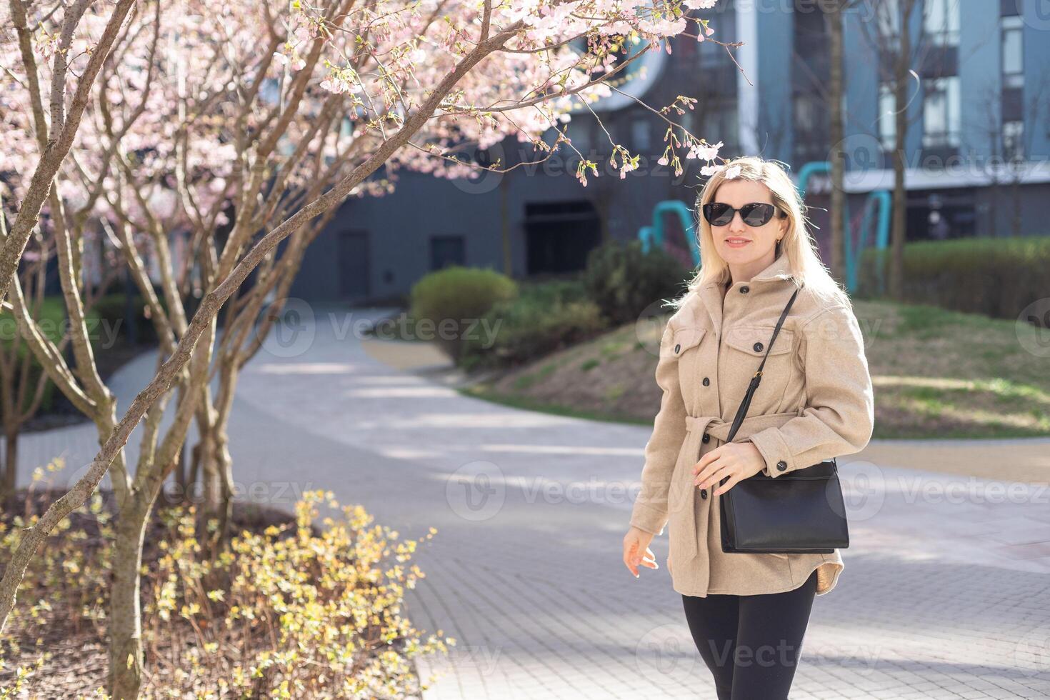 Blonde touches a branch of blooming cherry standing in the park photo