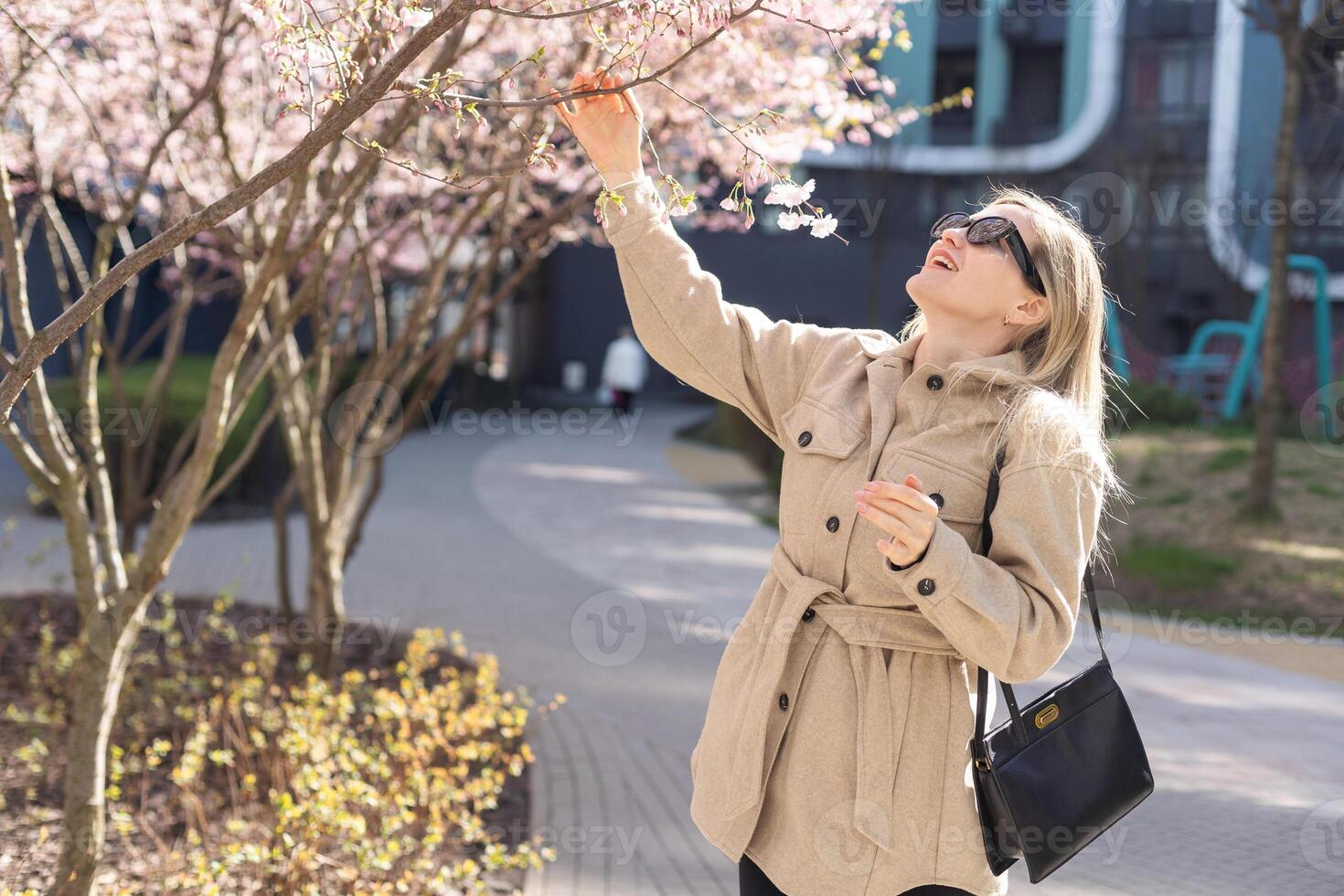 Blonde touches a branch of blooming cherry standing in the park photo