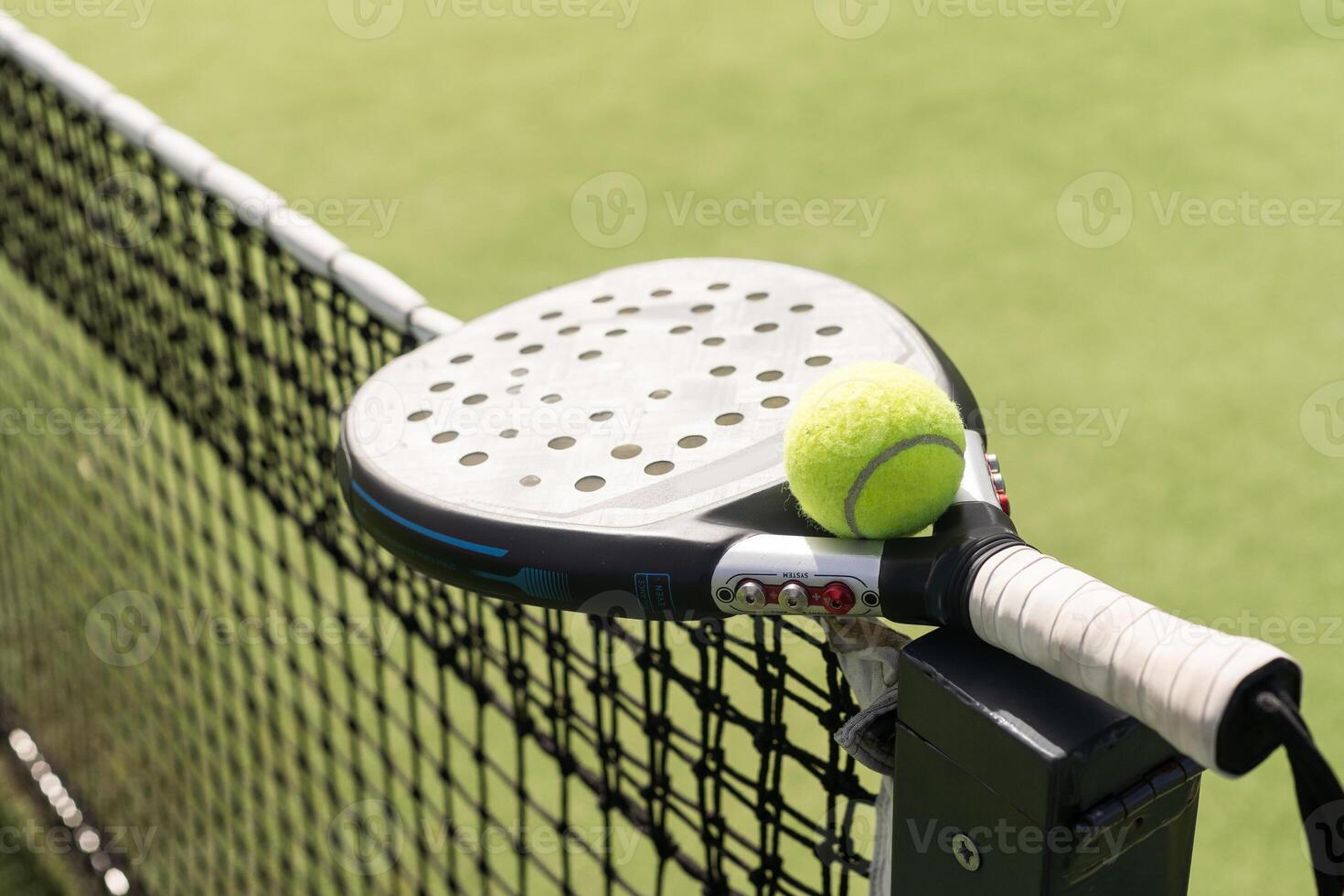 Padel racket and padel ball on a green court in the sunset photo