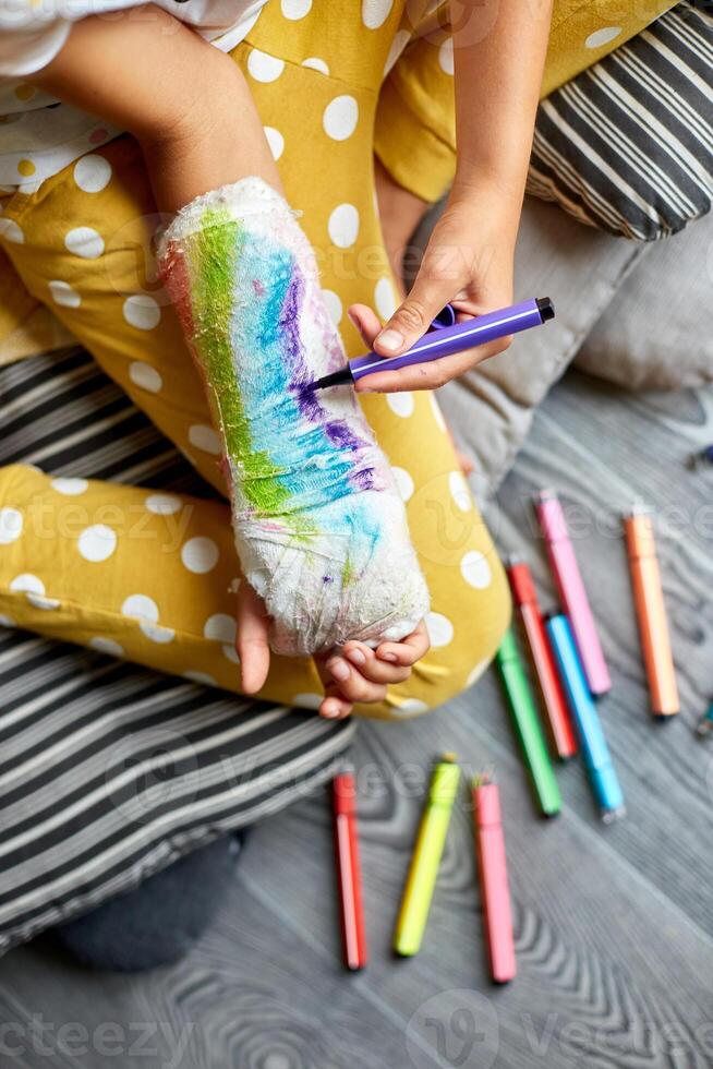 Teen girl with a broken arm at home draws an orthopedic cast photo