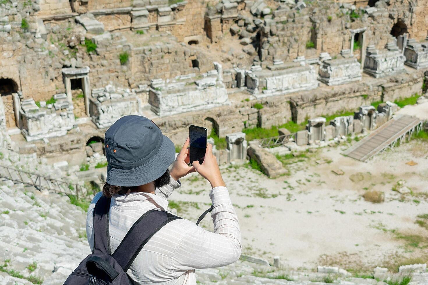 A male tourist enjoys a walk through the amphitheater among the ruins of the ancient city of Perge, in Turkey. The tourist looks around the ancient city of Perge with fascination and takes photographs photo