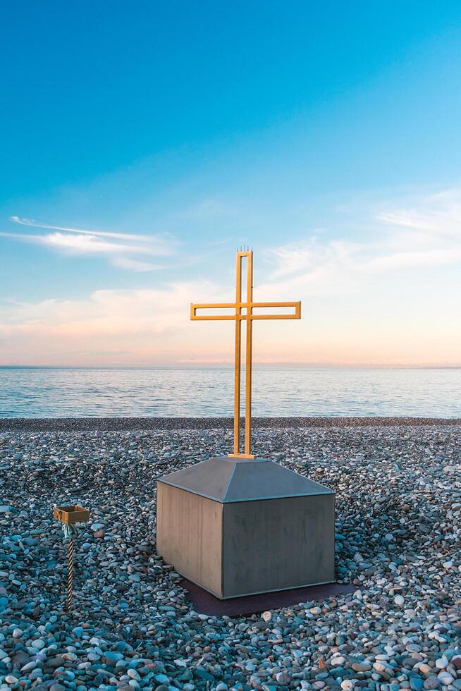 Golden cross on the sea and blue sky. A minimalistic view of a golden cross against the backdrop of a cloudy horizon. photo