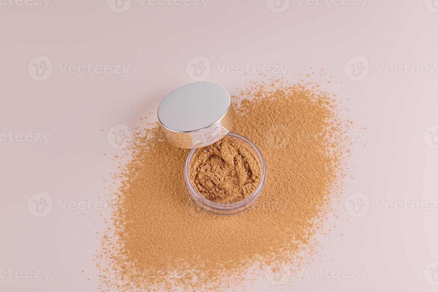 Top view of an open jar with loose powder of beige, bronze tone stands on a scattered sample of powder. A copy of the space. Make up. photo
