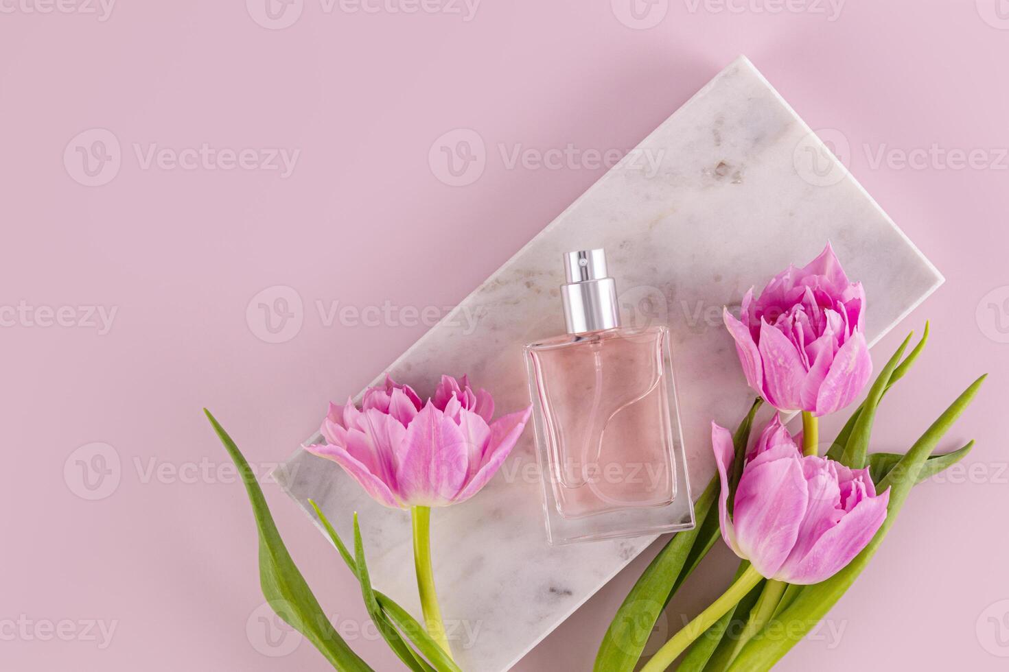 An elegant bottle of eau de parfum or women's perfume lies on a marble rectangular podium with tulips. Fragrance presentation. Top view. photo