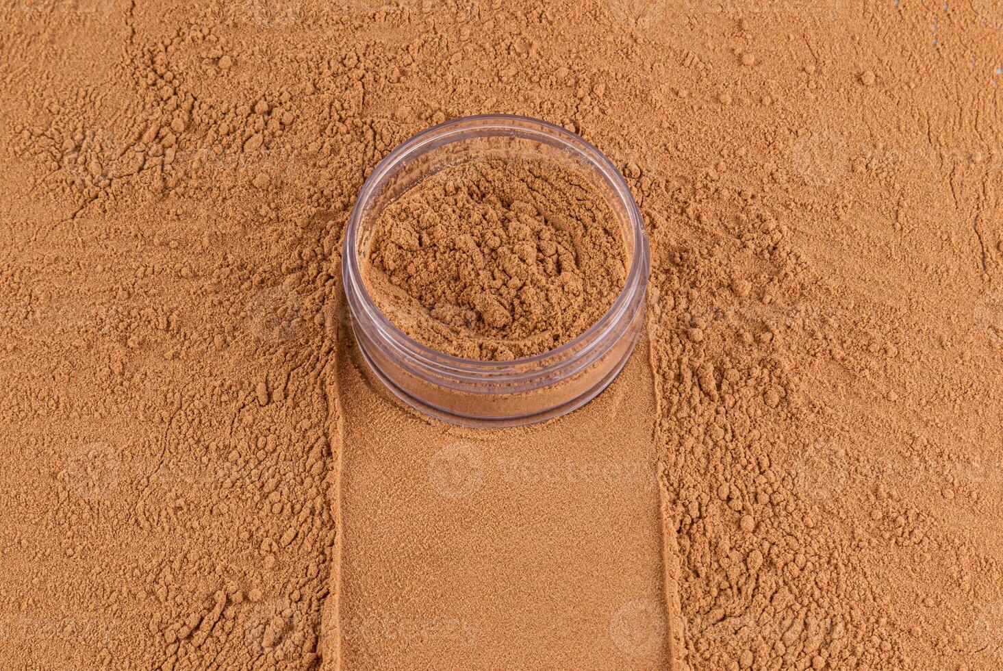 an open jar with loose powder of bronze tone stands on a scattered sample of powder. A copy space. Concept of cosmetics , make up. Top view photo