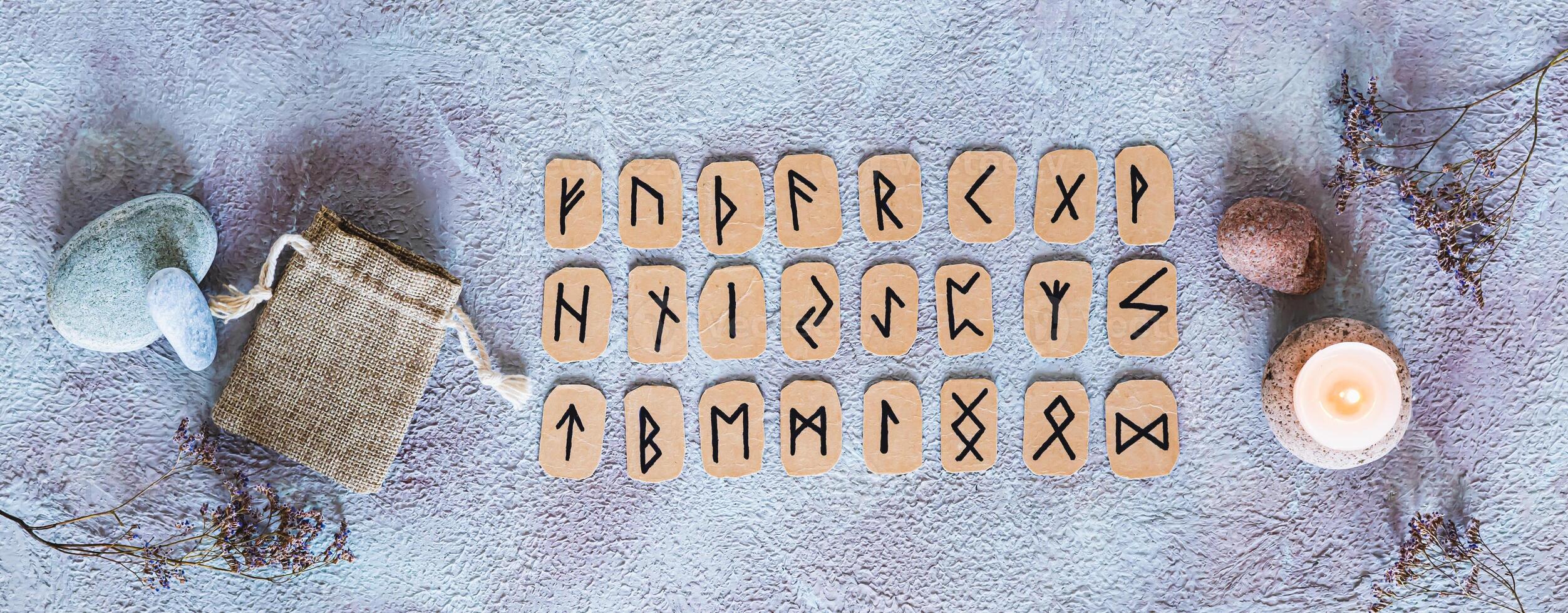 Scandinavian runes for fortune telling, pouch and candle on the table top view web banner photo