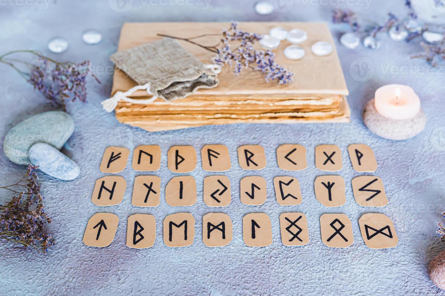 Scandinavian runes for fortune telling are in three rows, a book, stones and a candle on the table photo