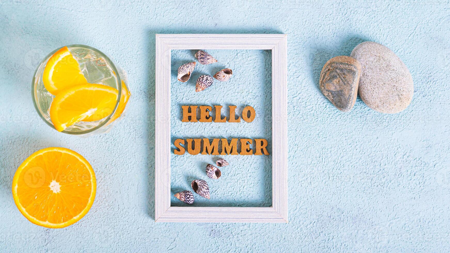 Hello summer text and seashells in photo frame, cocktail and orange on blue top view web banner