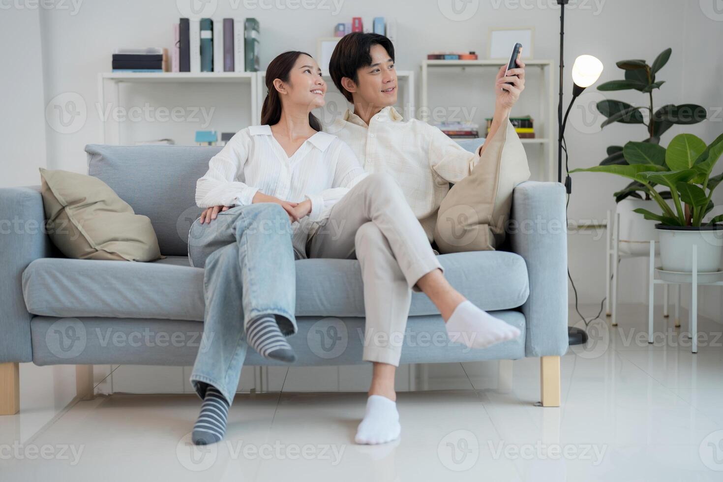 Couple relaxing on couch adjusting air conditioner with remote control photo