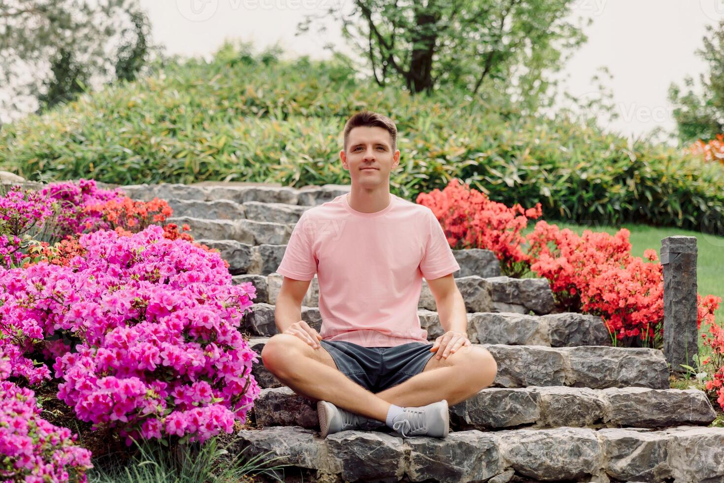 Young positive man sitting on stairs in summer garden. photo