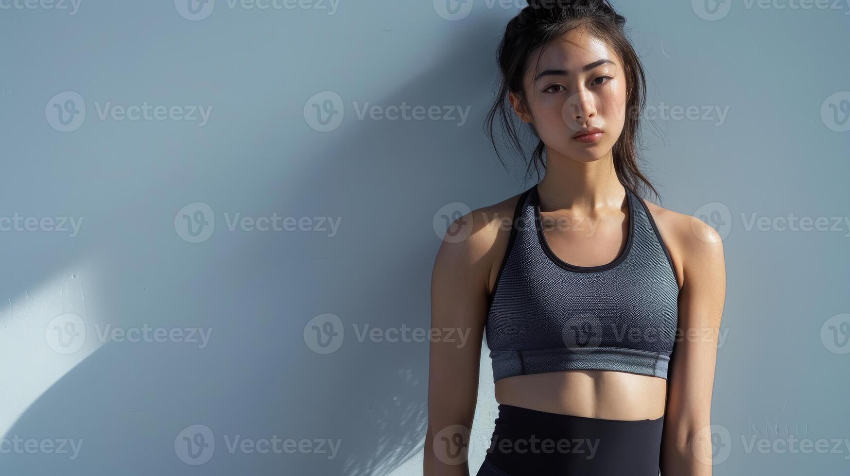 A woman in a sports bra and leggings poses in front of a wall photo