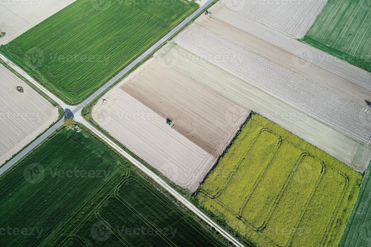 Aerial view from the drone, a bird's eye view of agricultural fields with a road through and a tractor on it in the spring photo