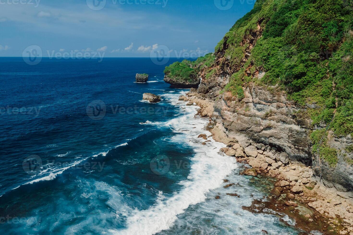Coastline with rocks and transparent ocean with waves in Bali. Aerial view. photo