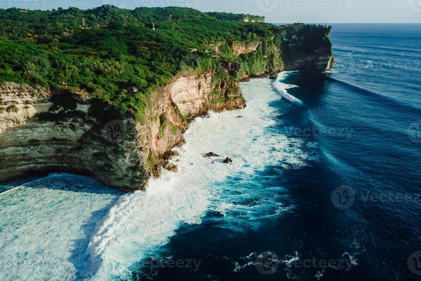 Rocky cliff coastline and ocean with waves near Uluwatu temple in Bali photo