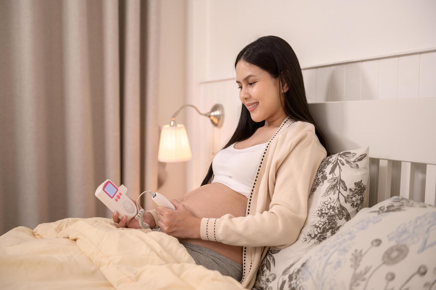 Beautiful pregnant woman holding pocket fetal doppler to listen baby's heartbeat on belly, fertility infertility treatment, IVF, future maternity concept photo