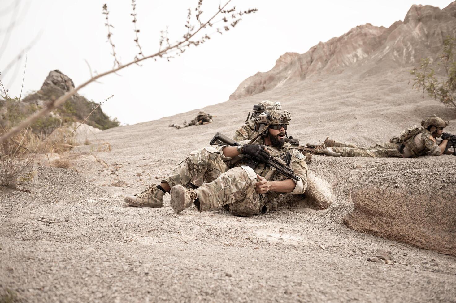 Soldiers in camouflage uniforms aiming with their rifles ready to fire during military operation in the desert , soldiers training in a military operation photo