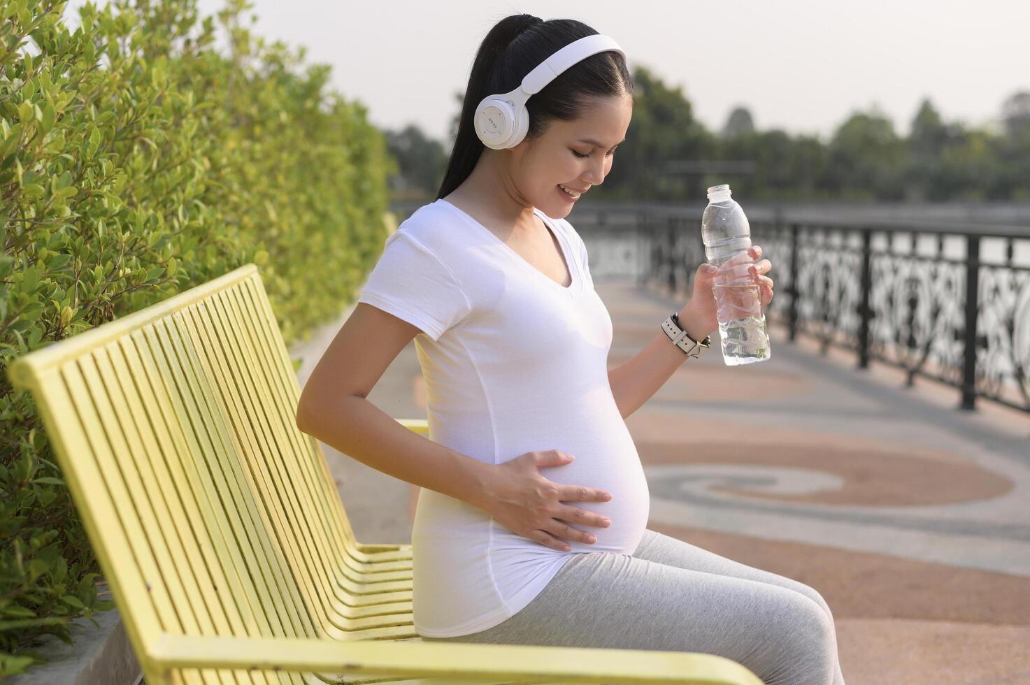 Beautiful pregnant woman drinking bottle of pure water in the park, Healthy and active pregnancy lifestyle concept. photo