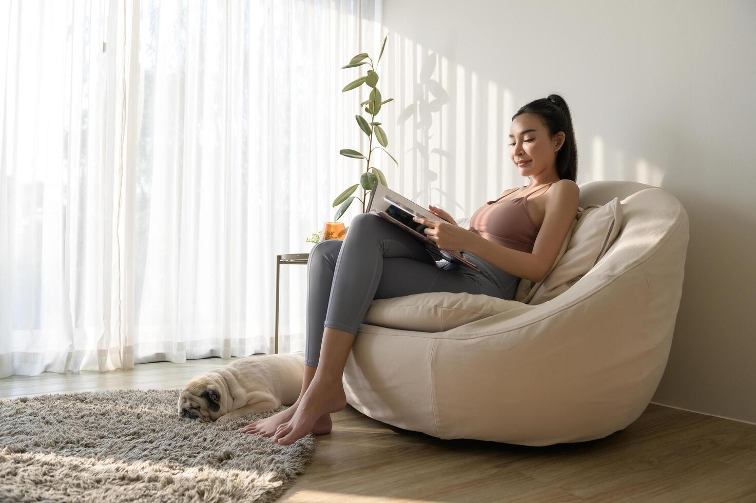 Young asian woman reading book with pug dog in living room at home photo