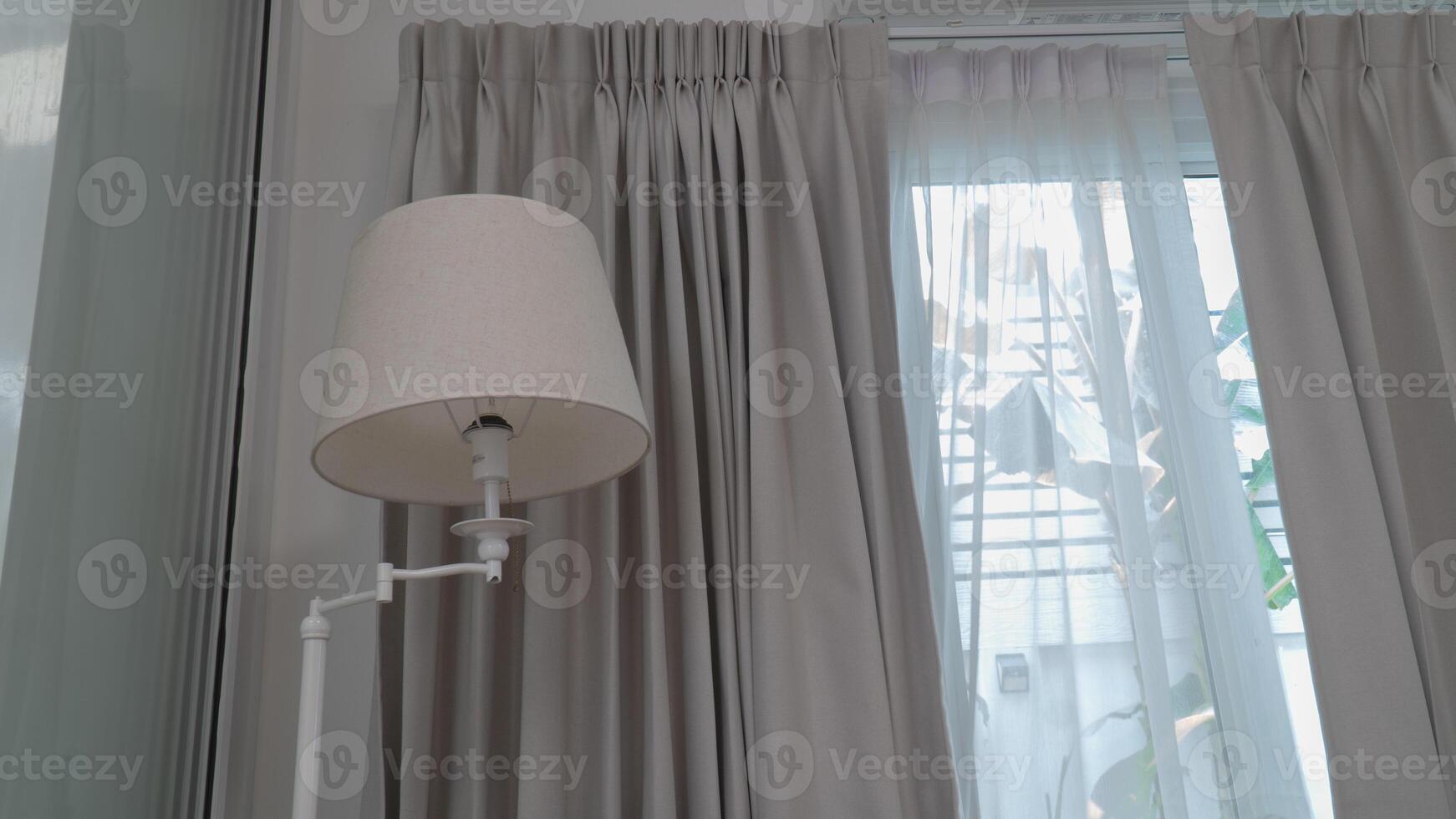 A floor lamp and a sheer curtain in front of a window photo