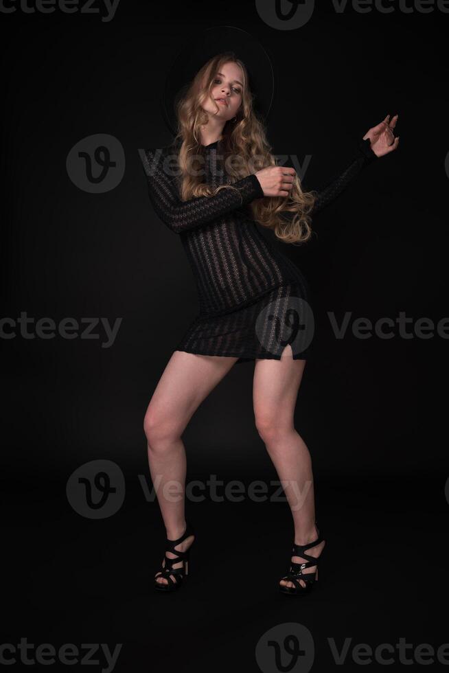 Woman is captured in full length portrait, posing with arms raised to side and gaze fixed downward photo