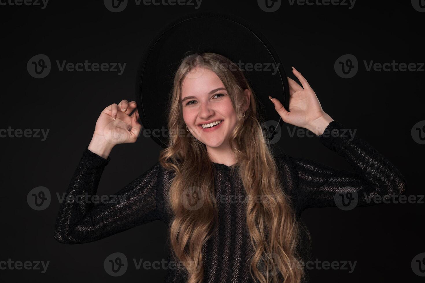 Portrait happy woman with toothy smile looking at camera, holding brim of felt hat with both hands photo