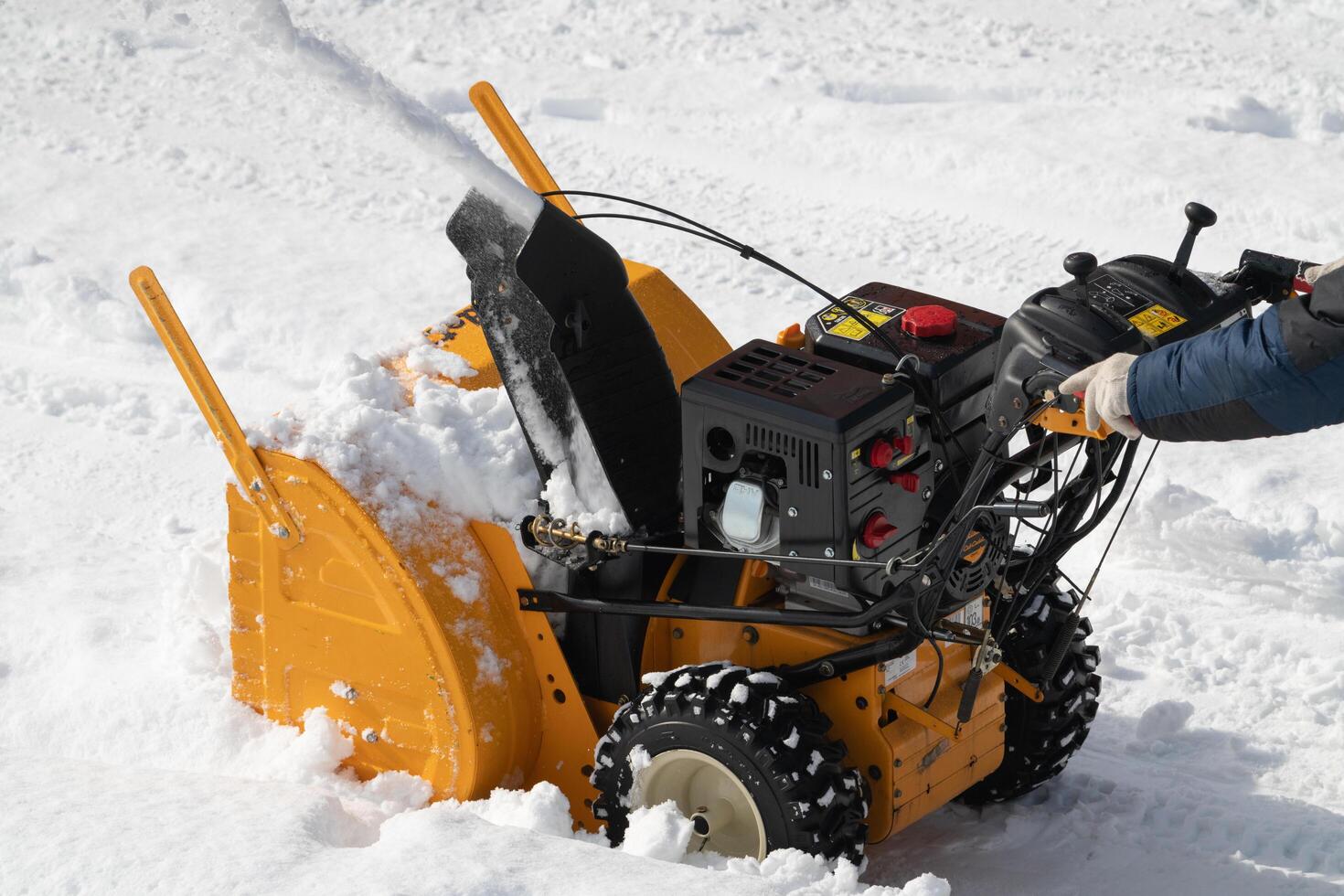 Worker is using snowblower machine to clear snow from parking after winter hurricane on sunny day photo