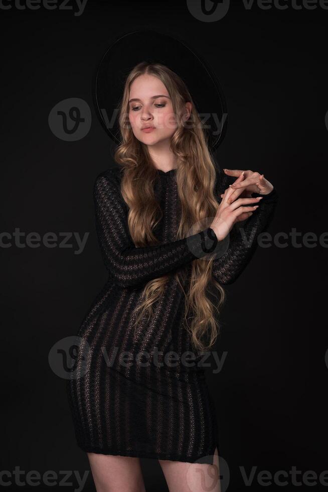 Portrait shy young blonde looking down and crossing arms shyly at elbows, poses on black background photo
