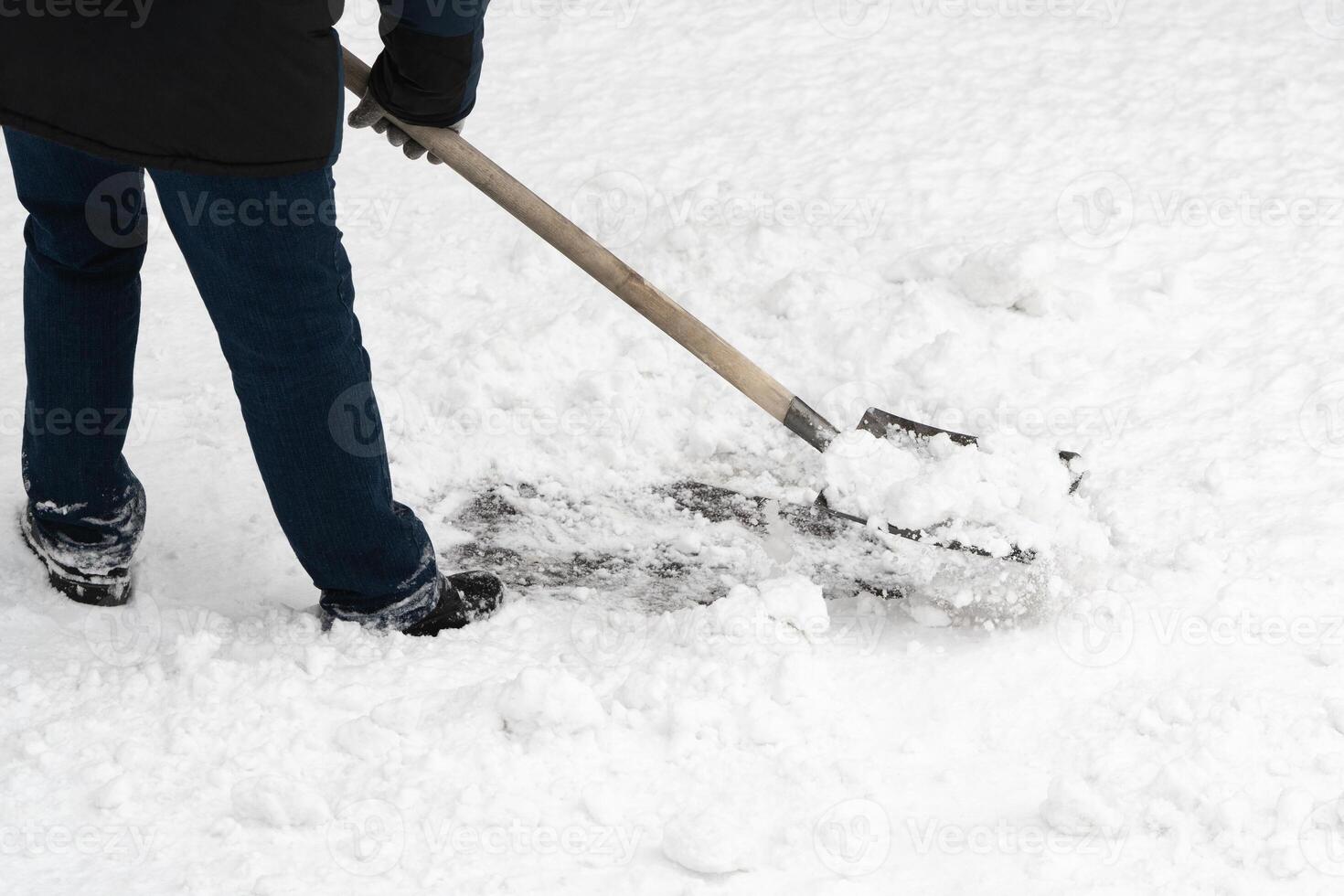 A man clearing away the freshly fallen snow with trusty iron shovel, complete with a wooden handle photo