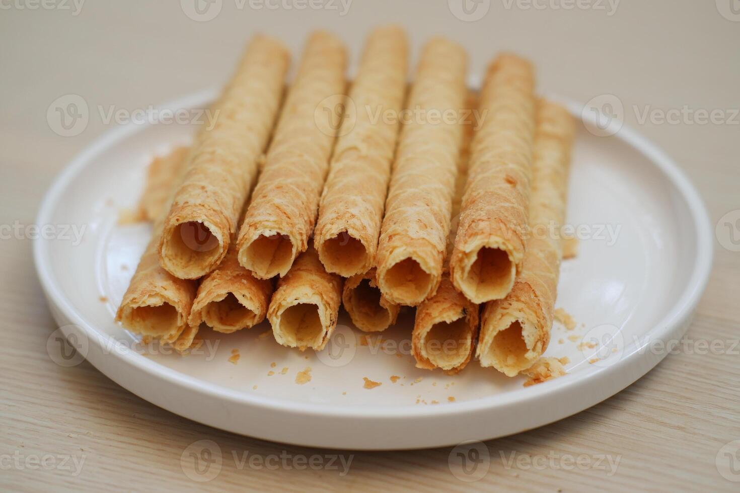 Pile of Cigarette Russe rolled biscuits on white plate on wooden table. photo