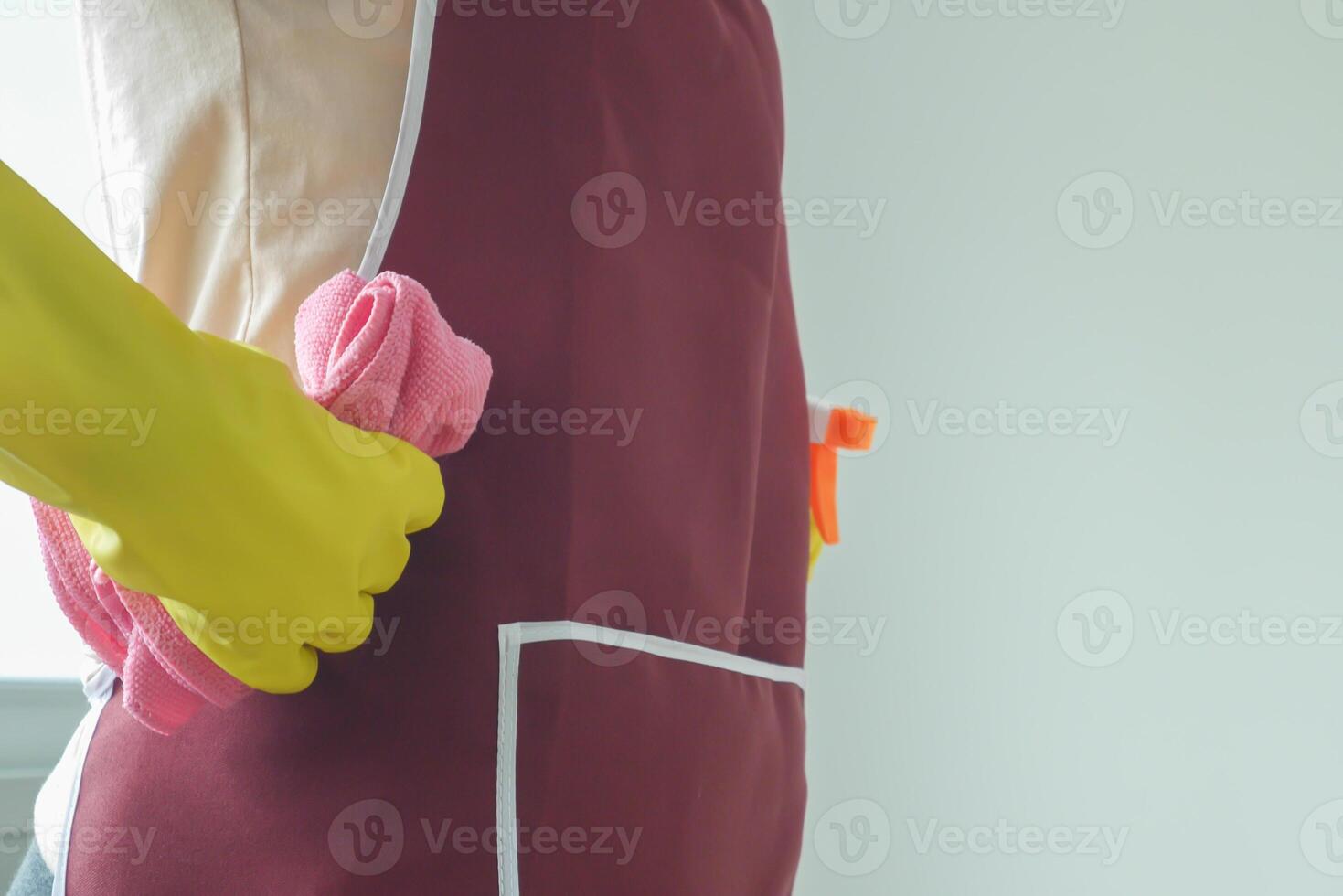 woman in a yellow apron is holding a pink towel and a bottle of cleaner. Concept of cleanliness and organization, as the woman is likely preparing to clean or tidy up a space photo